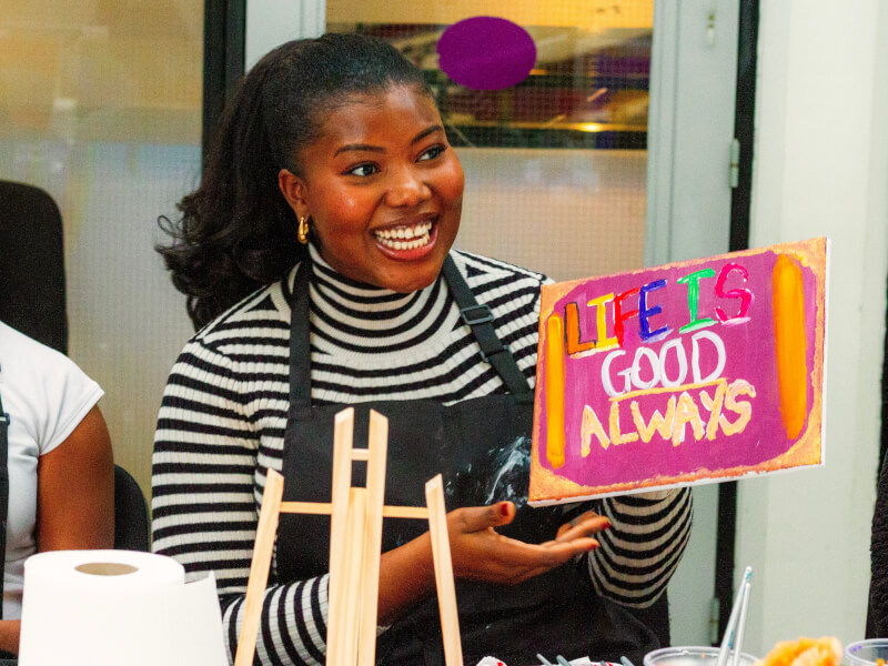 A student at a paint and sip class holds up their colourful work